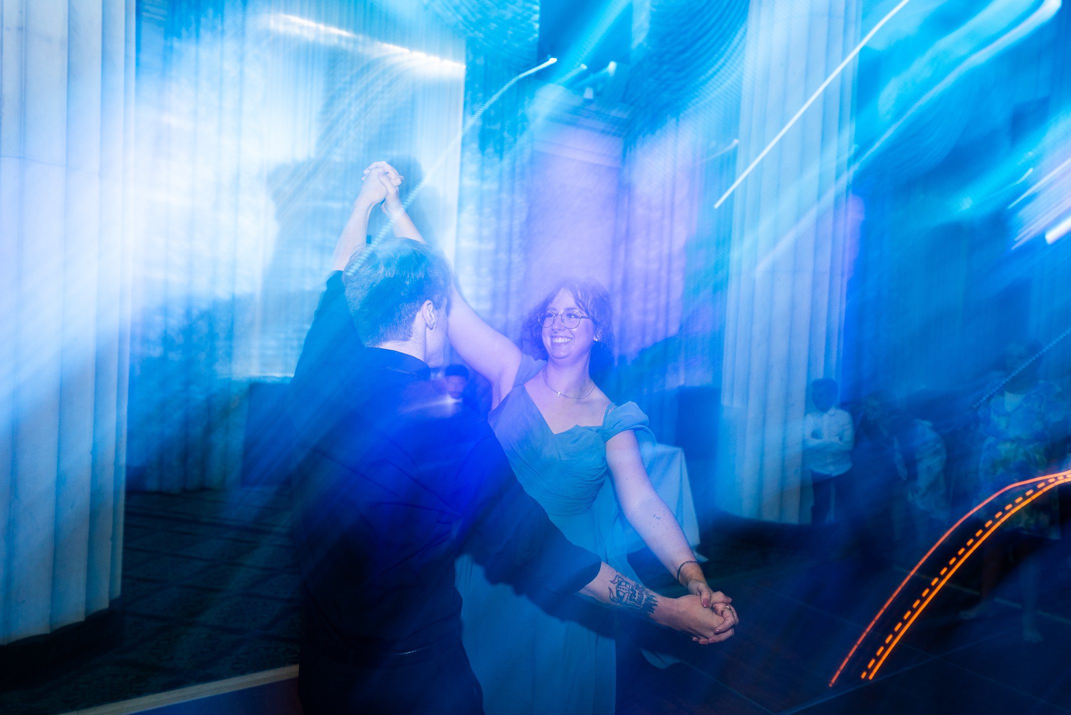 Guests dance beneath blue reception lights and sweeping motion
