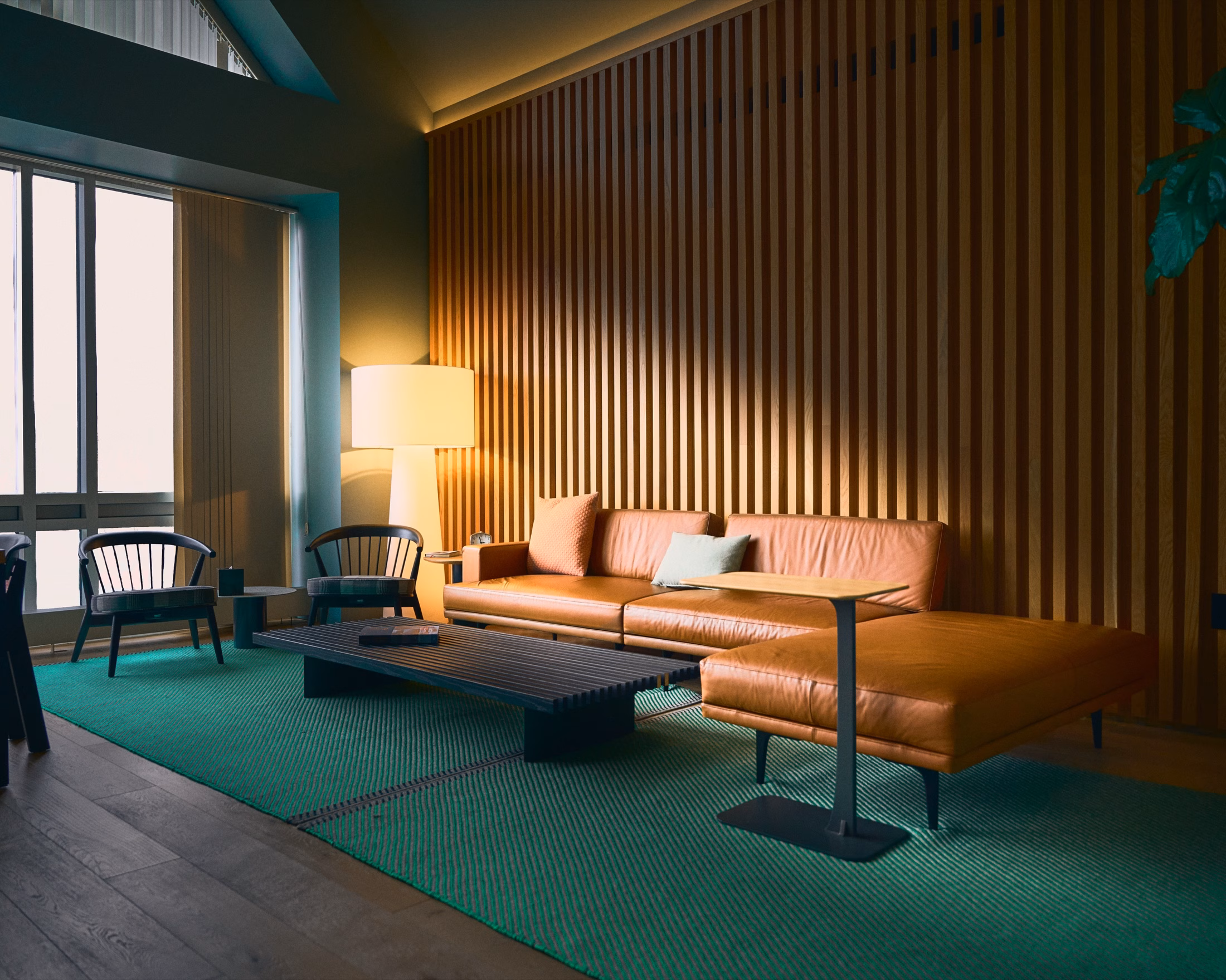 A warmly lit modern lounge with leather seating, wood slat walls, and a green rug